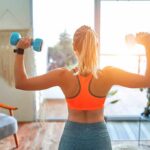 Woman lifting dumbbells at home gym near window