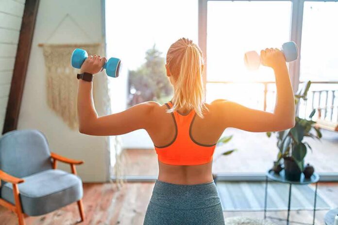 Woman lifting dumbbells at home gym near window