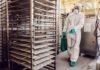 Worker in hazmat suit disinfecting industrial kitchen racks