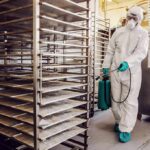 Worker in hazmat suit disinfecting industrial kitchen racks