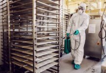 Worker in hazmat suit disinfecting industrial kitchen racks