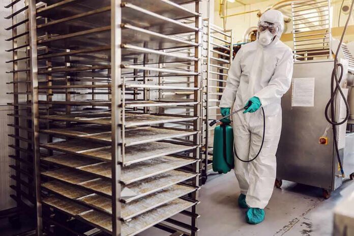 Worker in hazmat suit disinfecting industrial kitchen racks