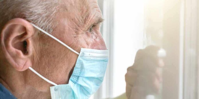 shutterstock_1879623874 Older man wearing a surgical mask looking out a window