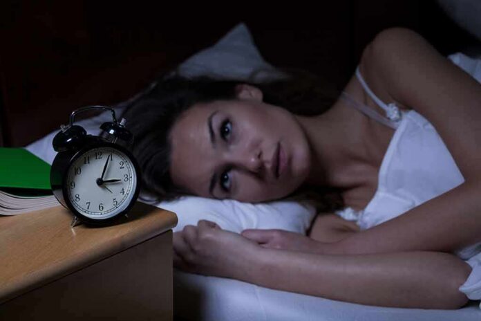 Woman lying awake in bed beside an alarm clock
