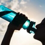 Silhouette person drinking from a blue water bottle
