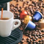 Espresso machine pouring coffee into a white cup with coffee pods and beans