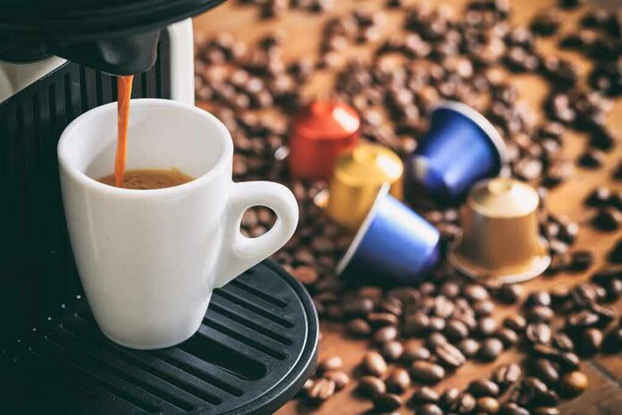 shutterstock_532833922 Espresso machine pouring coffee into a white cup with coffee pods and beans