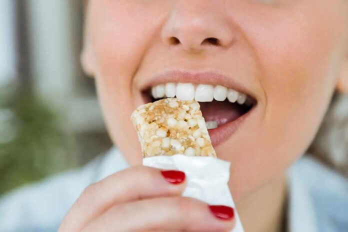 shutterstock_564161623 Person taking a bite of a granola bar