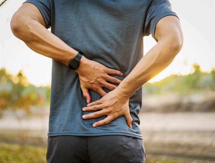 shutterstock_1020731773 Person holding lower back in pain outdoors