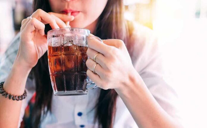 shutterstock_1033381774-1 person sipping iced drink from a glass mug with a straw