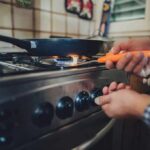 Person lighting a gas stove under a frying pan