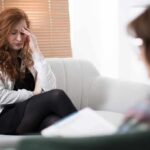 Woman with hand on forehead sitting on couch during counseling session