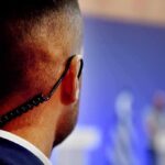 Security guard with earpiece watching a blurred event stage