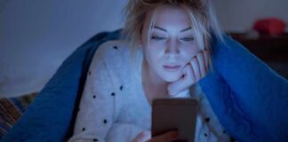Woman under a blanket looking at a smartphone in bed