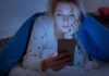 The 20-Minute Insomnia Rule: Get Out of Bed to Sleep Woman under a blanket looking at a smartphone in bed