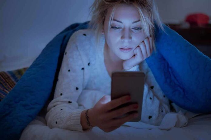 shutterstock_1129353881 Woman under a blanket looking at a smartphone in bed