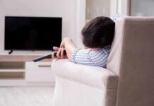 Irregular Sleep Tied To Dozens Of Illnesses Person lying on a sofa holding a TV remote