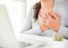 Research Just Linked Breast Size To 4 Health Conditions person clutching chest with both hands at a desk