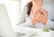 Research Just Linked Breast Size To 4 Health Conditions person clutching chest with both hands at a desk