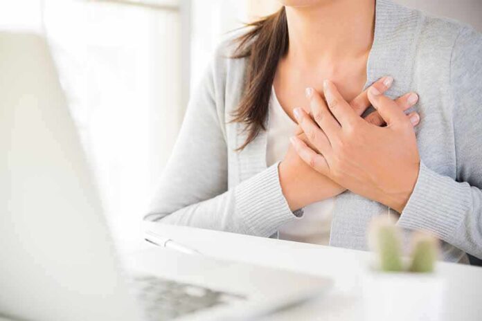 shutterstock_1176172219 person clutching chest with both hands at a desk
