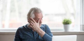 Older man rubbing his eye while sitting at a laptop