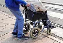 Caregiver pushing person in wheelchair over curb