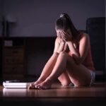 Woman sitting on floor covering face beside a bathroom scale