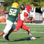 Football player in red runs with the ball as defender in green attempts a tackle