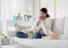 Woman sneezing on a sofa with tissues and a blanket