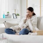 Woman sneezing on a sofa with tissues and a blanket