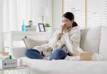 Woman sneezing on a sofa with tissues and a blanket