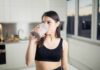 Woman in sportswear drinking a smoothie in a kitchen