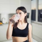 Woman in sportswear drinking a smoothie in a kitchen