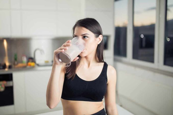 Woman in sportswear drinking a smoothie in a kitchen