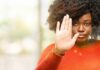 Woman in orange sweater holding up hand in stop gesture