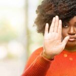Woman in orange sweater holding up hand in stop gesture