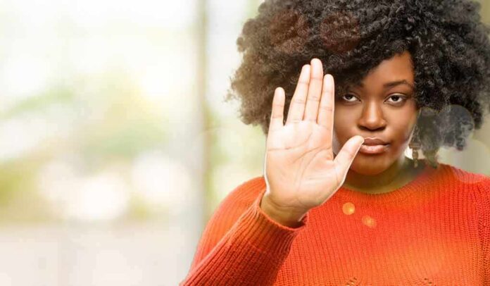 Woman in orange sweater holding up hand in stop gesture