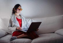 Why Some People Naturally Become Night Owls Person wearing orange glasses using a laptop on a white couch