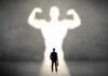 Businessman with briefcase casts a large muscular shadow on wall