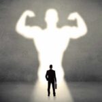 Businessman with briefcase casts a large muscular shadow on wall