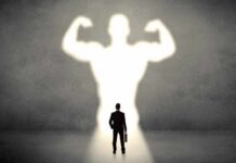 Businessman with briefcase casts a large muscular shadow on wall