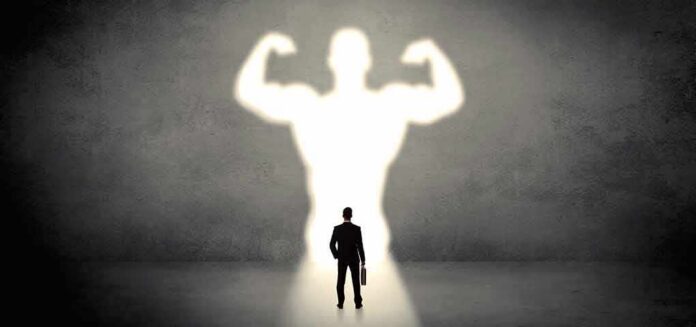 Businessman with briefcase casts a large muscular shadow on wall
