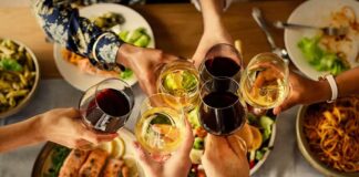 Hands clinking wine glasses over a dinner table