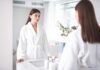 Woman in white bathrobe looking at herself in a bathroom mirror