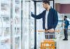 Man with shopping cart opens freezer door in grocery store