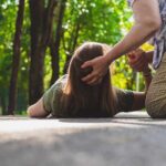 How to recognize the first signs of a stroke Person assisting someone lying on a path in a park