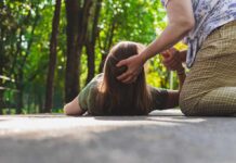 Person assisting someone lying on a path in a park