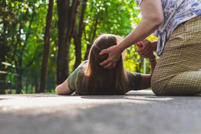 shutterstock_1462840388 Person assisting someone lying on a path in a park