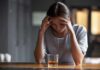 Addiction Cure? The Treatment Trap Woman with head in hands at a bar with a glass of whiskey