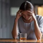 Addiction Cure? The Treatment Trap Woman with head in hands at a bar with a glass of whiskey
